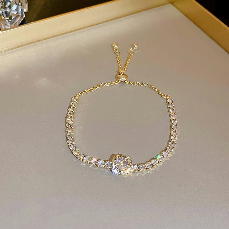 Pulseira ajustável "Aurum Diamond Halo" com design luxuoso. Possui um centro brilhante de zircônia cravejada, cercado por uma elegante fileira de pedras reluzentes que irradiam sofisticação. O ajuste deslizante proporciona conforto e praticidade, tornando-a perfeita para ocasiões especiais ou para elevar o seu estilo no dia a dia.