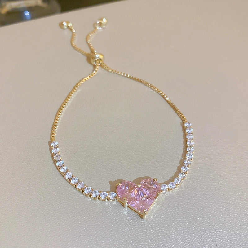 Pulseira "Aurum Royale Coração Rosé" – Um símbolo perfeito de amor e sofisticação. Esta delicada pulseira combina cristais brilhantes cravejados ao longo da corrente com um encantador coração rosé como peça central. Um acessório que mistura delicadeza e requinte, ideal para presentear ou realçar qualquer look com um toque romântico.