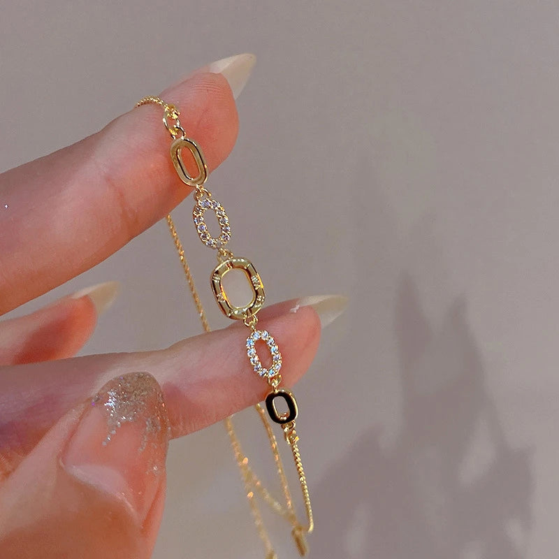 Pulseira "Aurum Royale Infinite Glam" – Um acessório delicado e versátil que combina formas geométricas entrelaçadas com detalhes cravejados de zircônias brilhantes. O design é moderno, destacando elegância e requinte, perfeito para mulheres que buscam complementar o visual com sofisticação em qualquer ocasião.