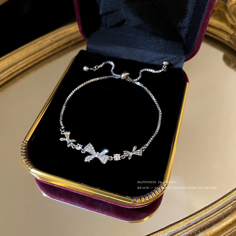 Pulseira ajustável "Elegância Aurum" com design delicado de laço cravejado de zircônias brilhantes. Essa peça apresenta um acabamento impecável, com detalhes em formas de flores que complementam o charme do laço central. Feita para destacar sua sofisticação em qualquer ocasião especial ou no dia a dia. Ideal para quem busca peças de joalheria com elegância e um toque de modernidade.